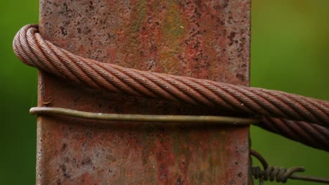 macro rusty texture, iron pillar with wire, steel cable and metal rebar, shallow focus against green background