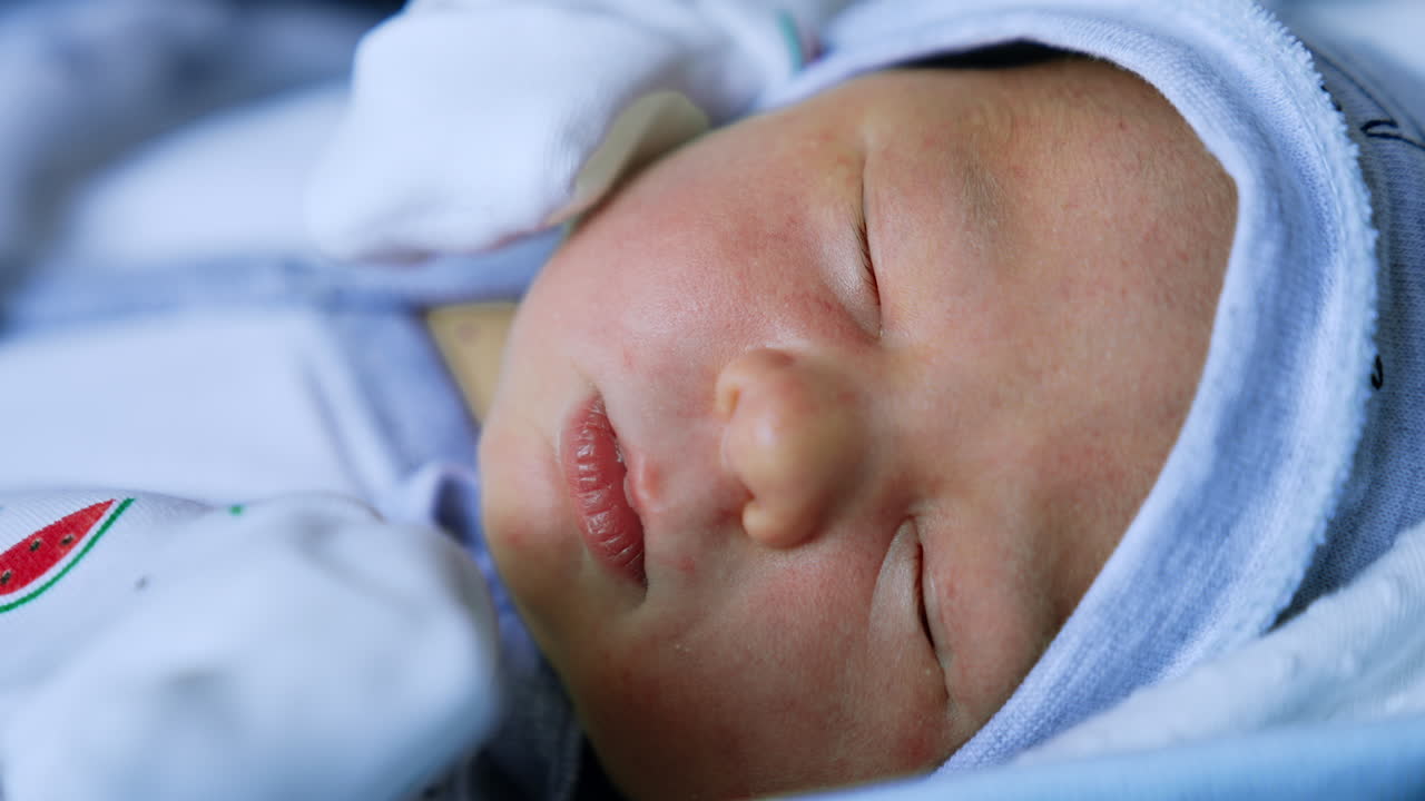 Face of a sleeping Caucasian newborn in cap. Little child sleeps tight close up.