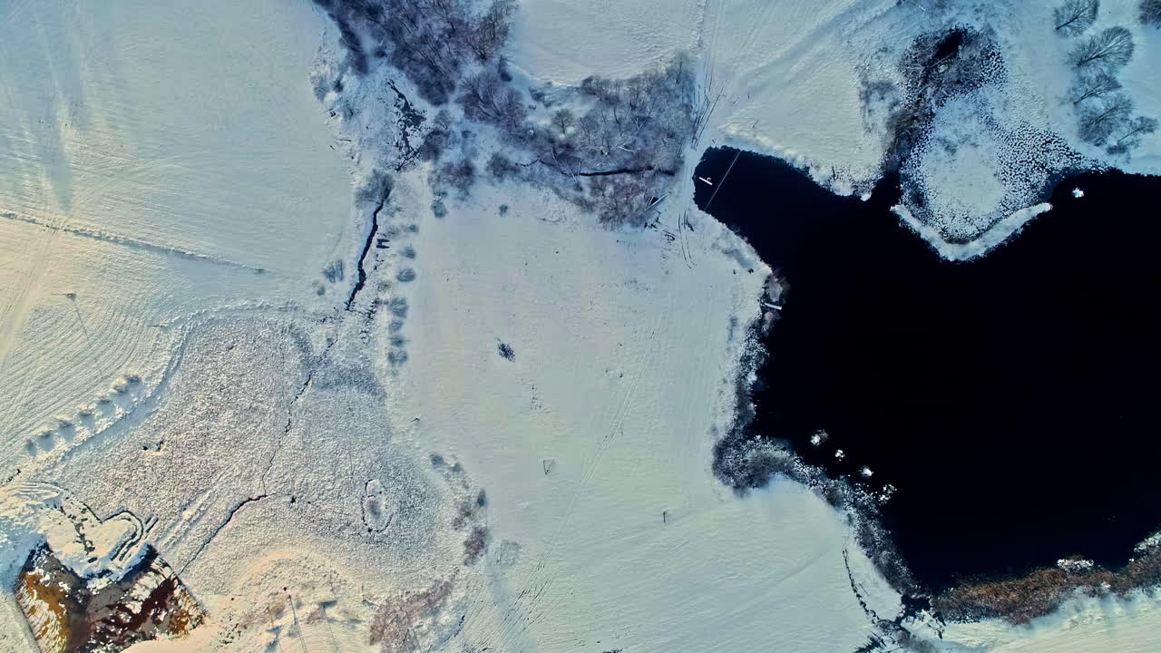un paisaje cubierto de nieve con un cuerpo de agua oscuro en contraste, vista aérea
