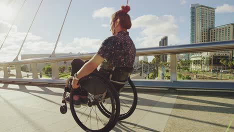 young happy disabled doing wheelie in wheelchair across bridge in city with lens flare