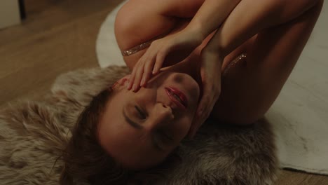 portrait of a beautiful young woman lying on a fur rug on the floor, she smiles and caresses her face