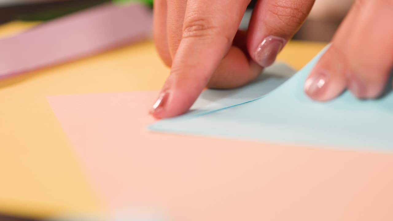 Primo piano di dita che piegano con precisione un foglio di carta blu per origami su un'area di lavoro luminosa