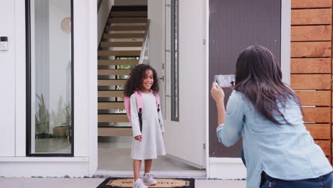 Madre-Tomando-Una-Foto-De-Su-Hija-Con-Un-Teléfono-Celular-El-Primer-Día-De-Regreso-A-La-Escuela