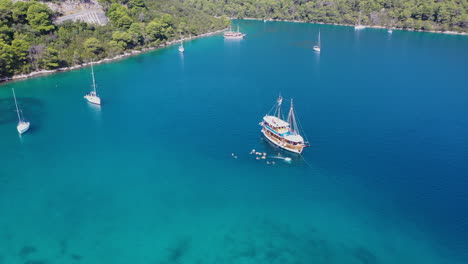 people swimming and jumping off sailboat in tropical sea, aerial arc shot