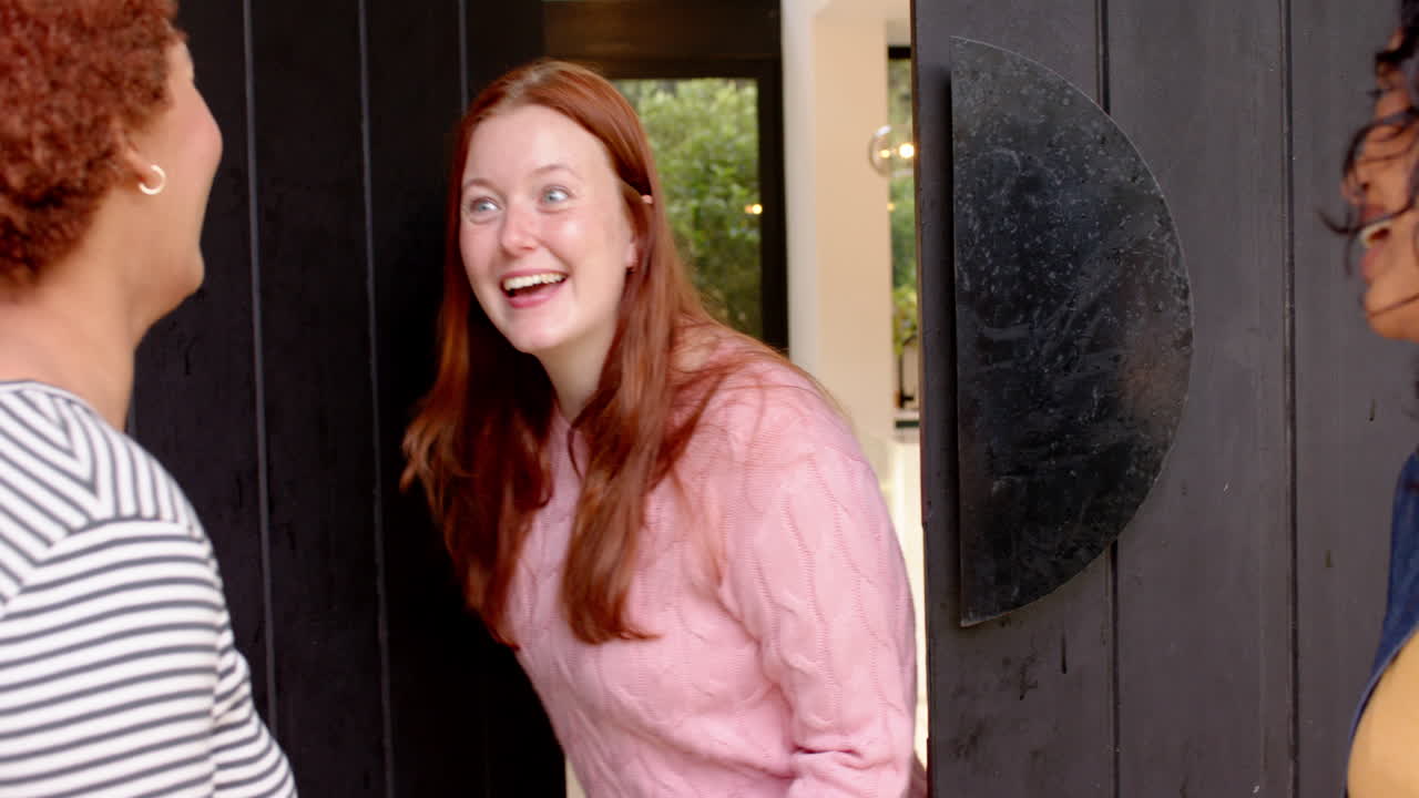 Hugging and smiling, diverse female friends greeting each other at home entrance