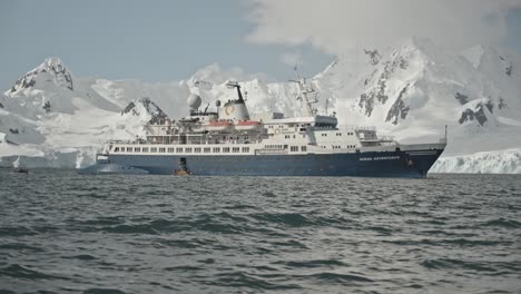 big blue and white ship in front of snow covered mountains in polar region