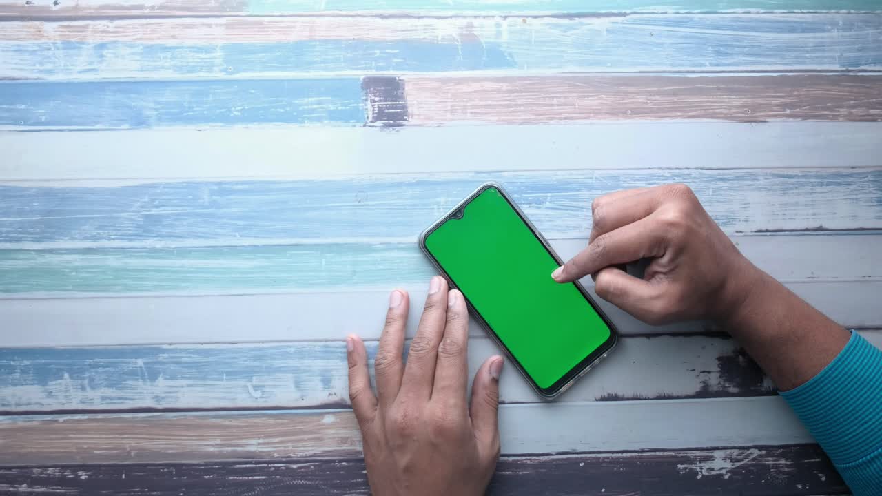 Persona che usa uno smartphone con schermo verde su un tavolo di legno