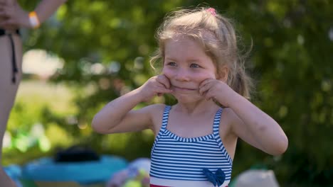 Close-up-Little-girl-child-in-bathing-suit-imitates-smile-stretches-her-lips-with-her-hands-poses