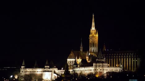 Vista-Del-Centro-De-La-Ciudad-De-Budapest-Y-El-Río-Danubio-Por-La-Noche,-Arquitectura-Gótica,-Reflejos-De-Luz,-Torre-De-La-Iglesia-Iluminada,-Plano-Medio-Distante