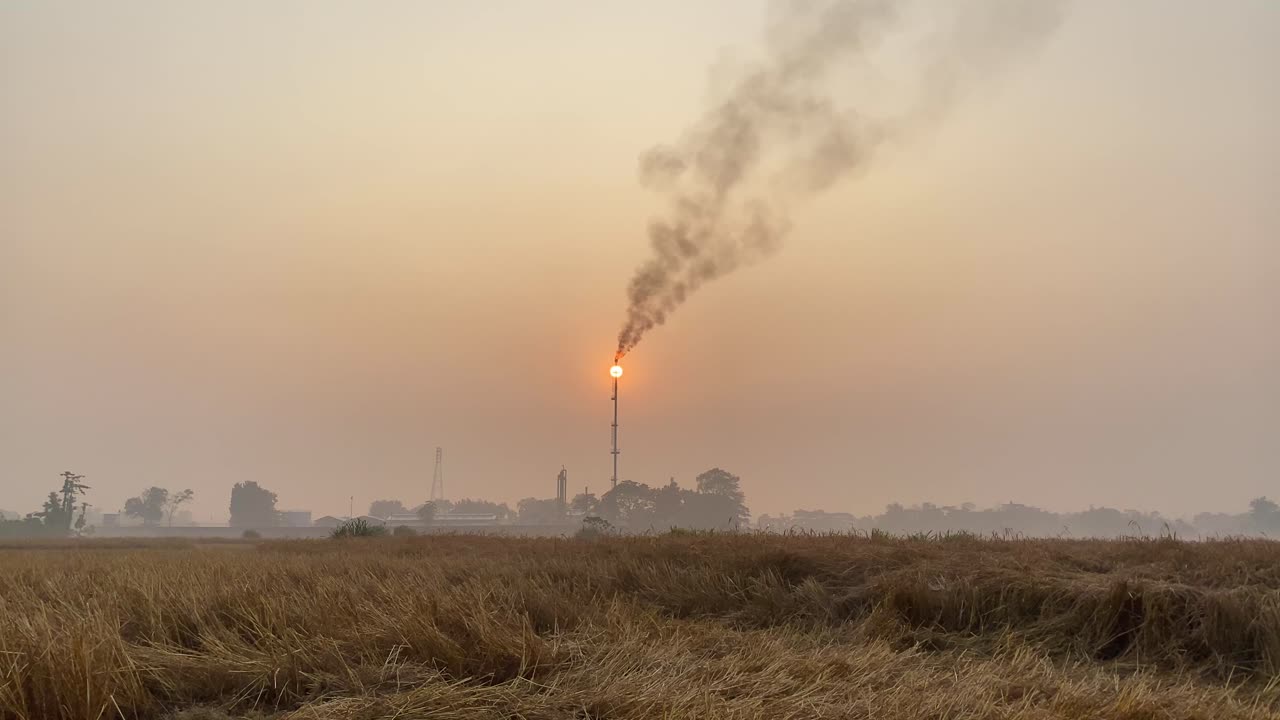 vista del fondatore statico dell'area industriale con la torre dell'impianto a gas che rilascia fumi inquinanti, cielo al tramonto nebbioso arancione