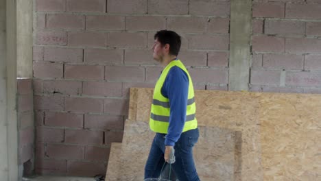 tomada amplia en cámara lenta de 4k de un trabajador que lleva dos cubos, filmada desde el lado con un cardán siguiendo paralelo al trabajador en un sitio de construcción