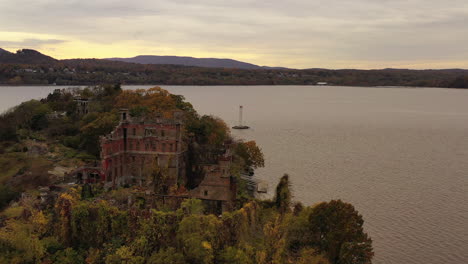 aerial drone camera flight towards bannerman's castle over the hudson river in beacon, ny on a cloudy, grey evening during sunset, the drone orbits right around the castle