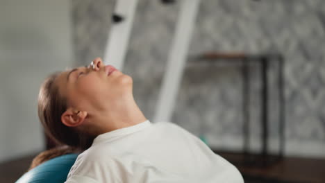 woman works on back muscles using fitness ball in residence room. calm lady in workout clothes finds pleasure in exercising on stability ball in home gym