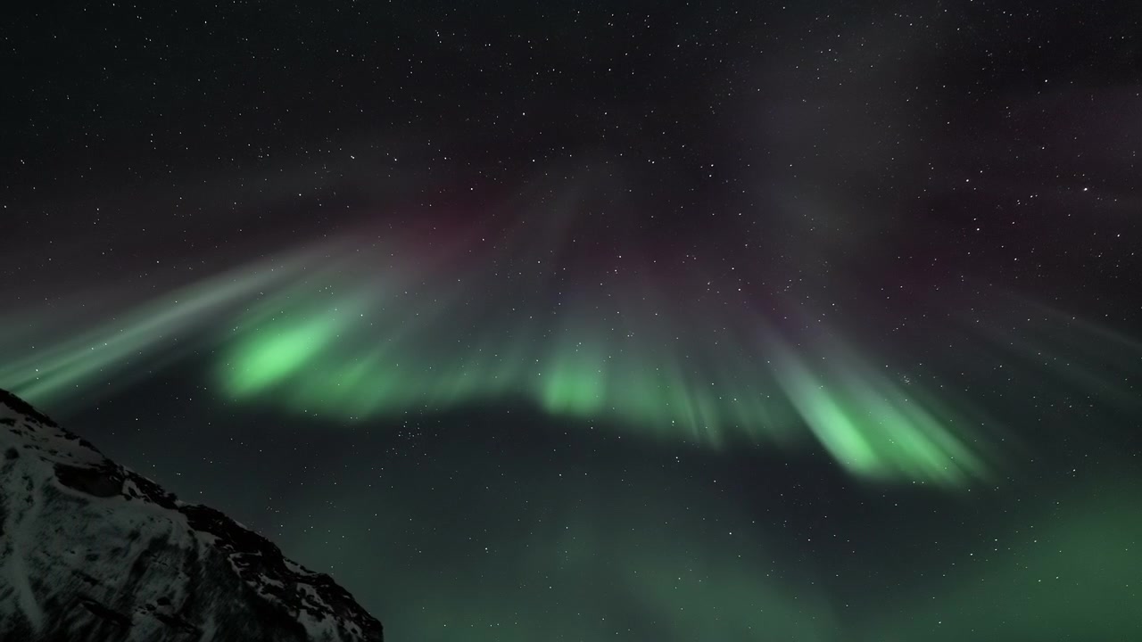 Vibrante Aurora Boreale che danza su una cima montuosa innevata di notte