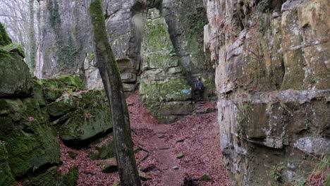 hombre caminando entre enormes formaciones rocosas y dando un descanso y tomando café en la ruta de senderismo mullerthal en luxemburgo - cámara al frente