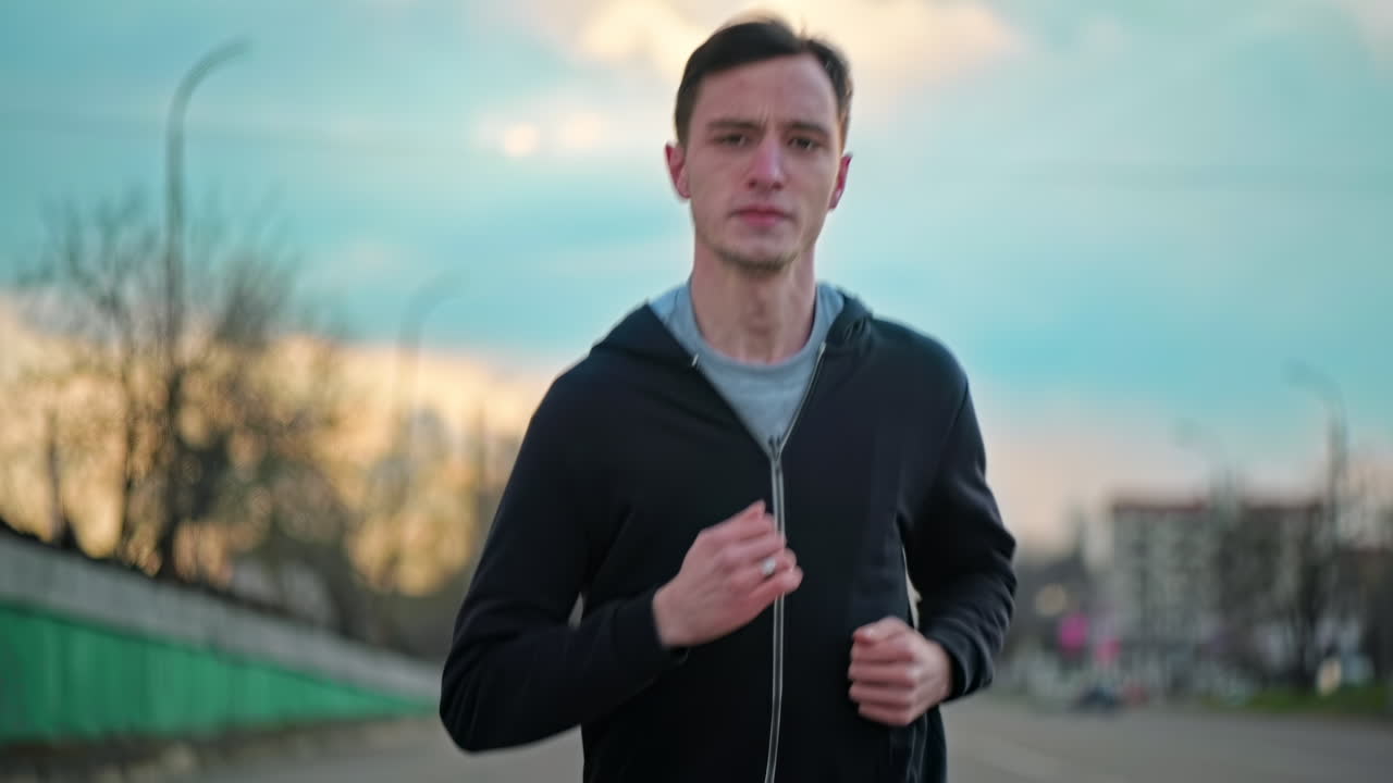 Young focused man running in jacket. Cloudy weather. Slow motion