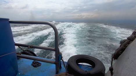 View-from-back-of-boat-looking-out-to-sea-as-smoke-from-engines-with-tire,railing-and-water-wake-on-sea-in-super-slow-motion-240fps-in-HD