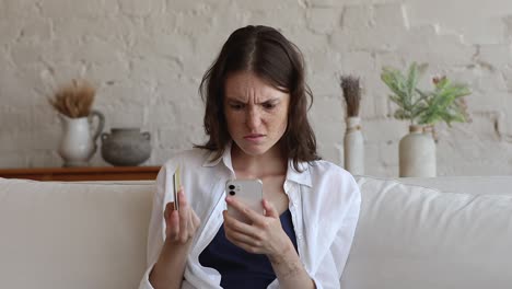 woman holding credit card and phone having troubles with payment