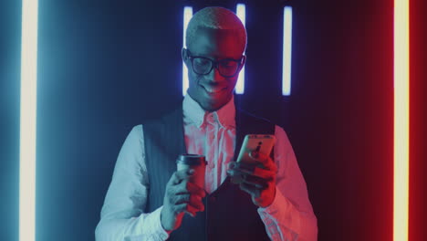 man using phone while drinking coffee in neon light