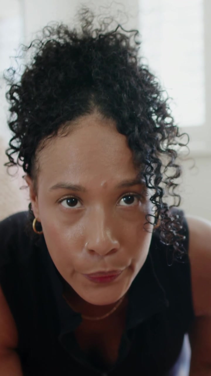 Adult woman leaning to low camera, holding gaze, showing hoops, making subtle shifts for marketing