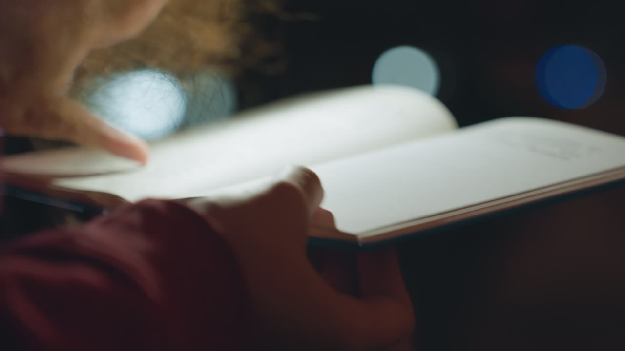 Closeup hands turning pages at night, curlyhaired writer flips journal under soft city bokeh and lamp glow, textured cover and inked margins, reflective solitude and gentle gestures