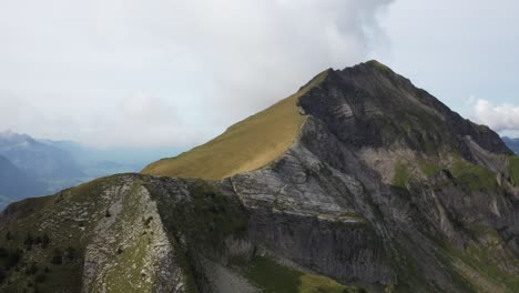 A-circling-drone-shot-moving-from-one-side-with-rocky-cliffs-to-the-other-with-lush-green-grass-with-the-ridge-of-Morgenberghorn,-Switzerland-in-between