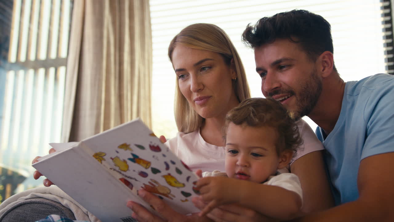 Famiglia seduta sul divano a casa con i genitori che leggono un libro con il figlio piccolo
