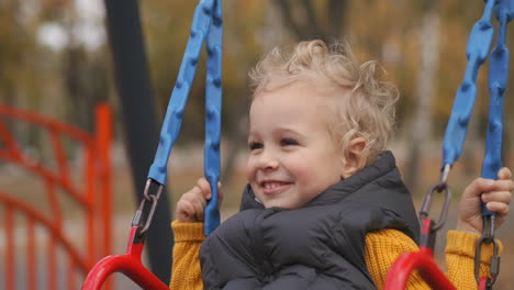 happy light-haired toddler is swaying on swing in park at autumn day portrait of happy and laughing child having fun baby