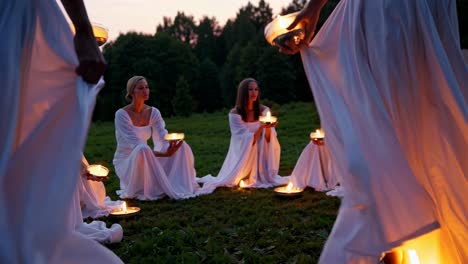 women in white dresses holding candles in a circle at sunset
