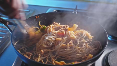 stirring chow mein noodles with ground turkey and vegetables cooked in a skillet