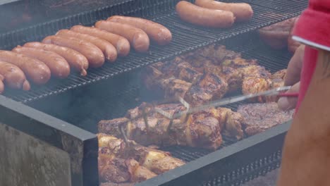man in the red t-shirt turns over the meat on the grill. he work outside.
