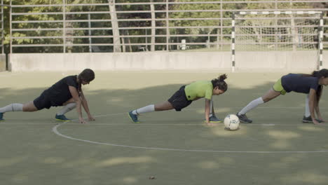 long shot of female football players lunging forward and stretching legs at the stadium