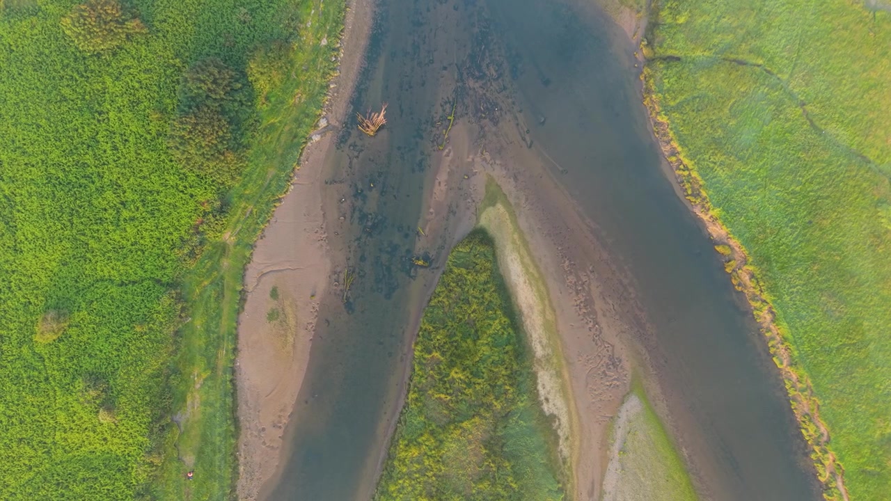 Vista aerea dall'alto del fiume Ogmore che si divide in una palude erbosa con una luce soffusa dell'ora d'oro.