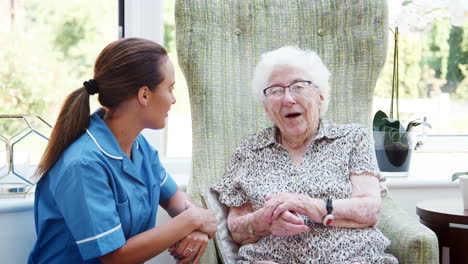 senior woman sitting in chair and talking with nurse in retirement home