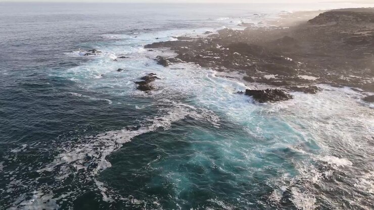 Acqua turchese dell'oceano e schiuma bianca delle onde si avvolgono attorno a una costa vulcanica nera e frastagliata, panoramica aerea statica