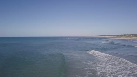 aerial flight over the sea, breaking waves and surfers in a very blue day