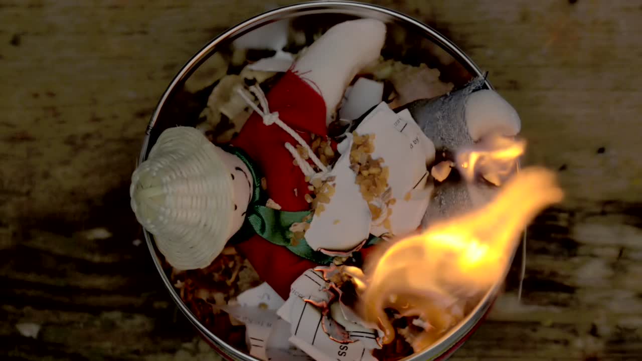 Sorcery witchcraft voodoo ritual with a doll being thrown out inside a bowl with fire to make a curse spell with him.  Muñeco de año viejo