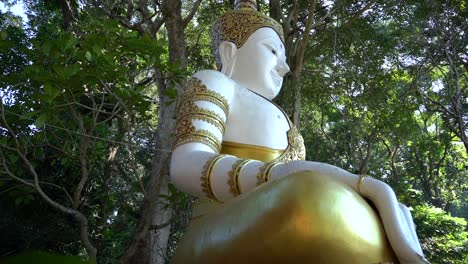 serene white and gold buddha statue in lush green forest