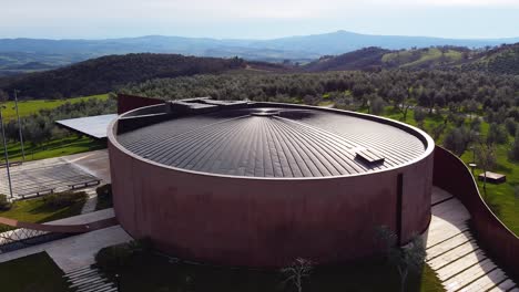 this aerial footage of montecucco captures the forum fondazione bertarelli surrounded by trees and vineyards. the camera performs a dolly movement to the right, revealing the scenic surroundings.