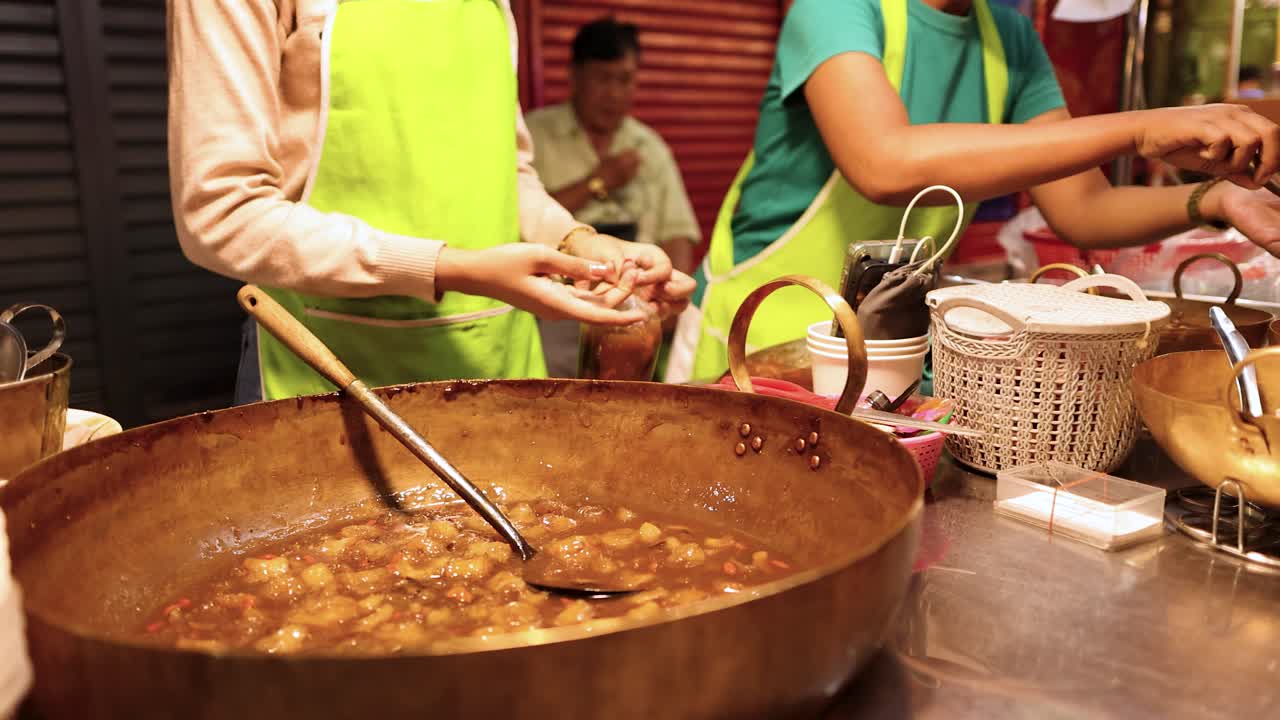 Vendors serve fish maw soup from a large pot at a bustling Bangkok street stall