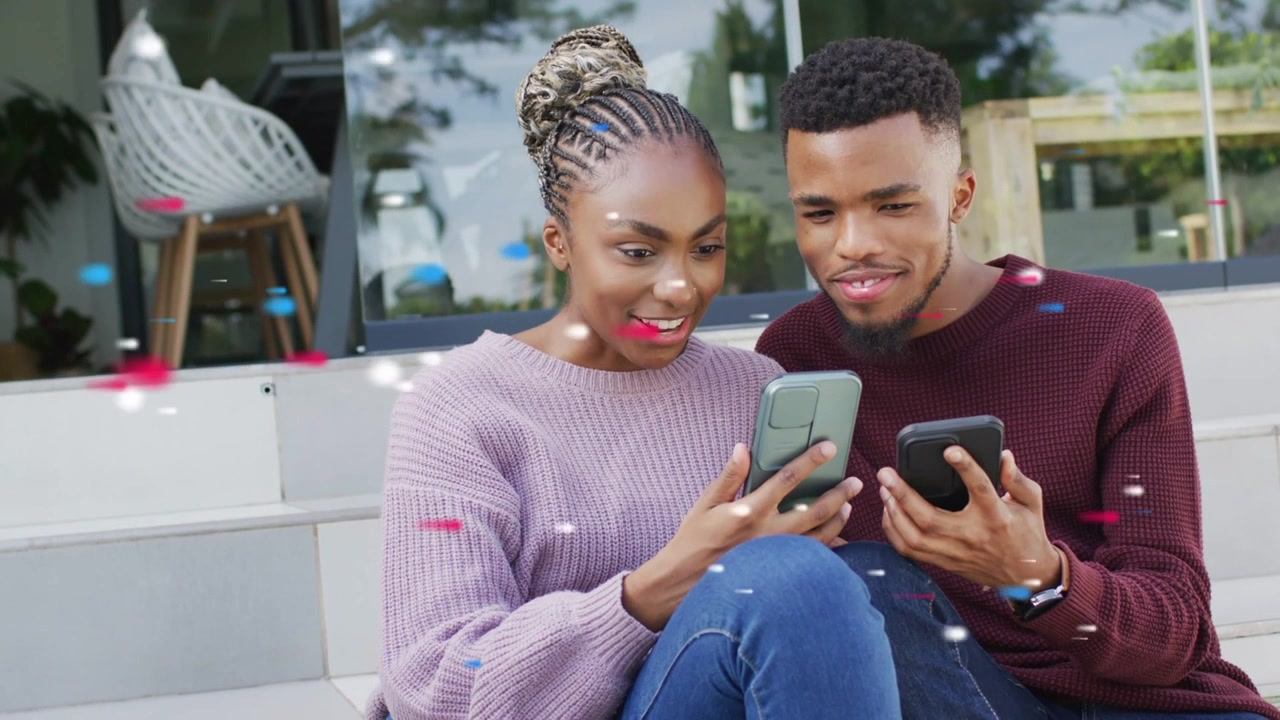 Woman tapping phone showing social post for fun on steps, man leaning in smiling, confetti drifting