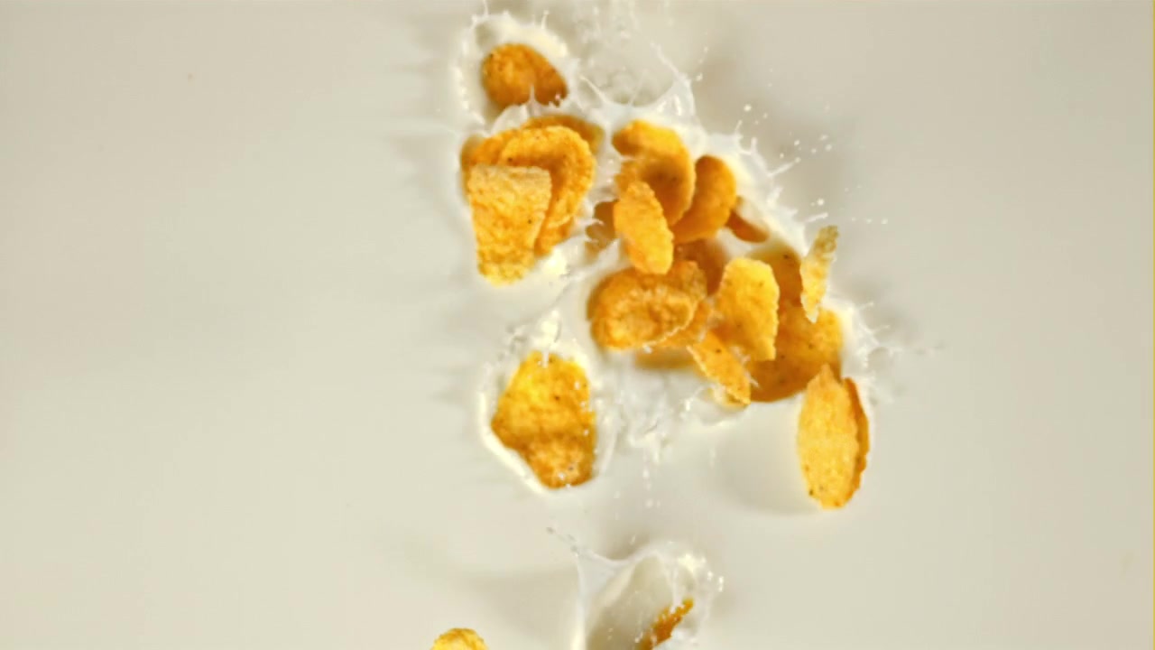 Slowmotion af gyldne cornflakes, der falder ned i mælk med sprøjt