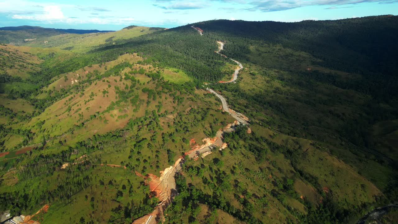 Una lenta ripresa aerea in avanti cattura il cielo blu vivido, le colline risplendenti, una strada incompiuta e i contorni perfetti delle montagne con il tempo sereno di Daang Kalikasan Aguilar Mangatarem Pangasinan, Filippine.