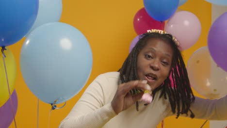 studio portrait of woman wearing birthday headband celebrating with balloons and party blower 1