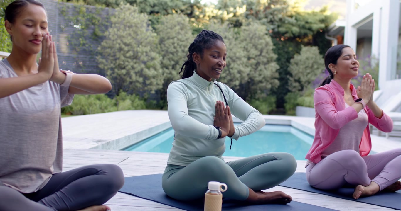 Guided cue Diverse female friends moving palms to chest on mats by pool with bottle centering