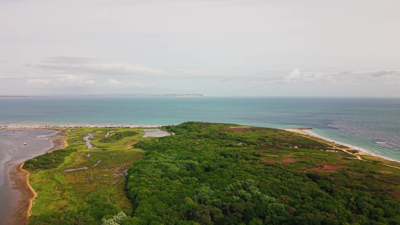 Drohnenaufnahme mit Blick über das Naturschutzgebiet Hengistbury Head mit Waldgebieten, Heidelandschaft, Feuchtgebieten, Hafenbooten, türkisfarbenem Meer und der fernen Küste der Isle of Wight.