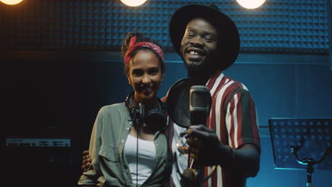 portrait shot of the mixed races stylish young man and woman, singers of the duo looking at each other and then smiling to the camera in the sound studio