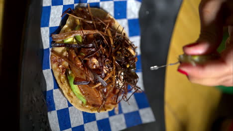 vertical slow motion of a seafood tostada with fried onion strips placed on a blue checkered paper and a woman squeezing a lime on top