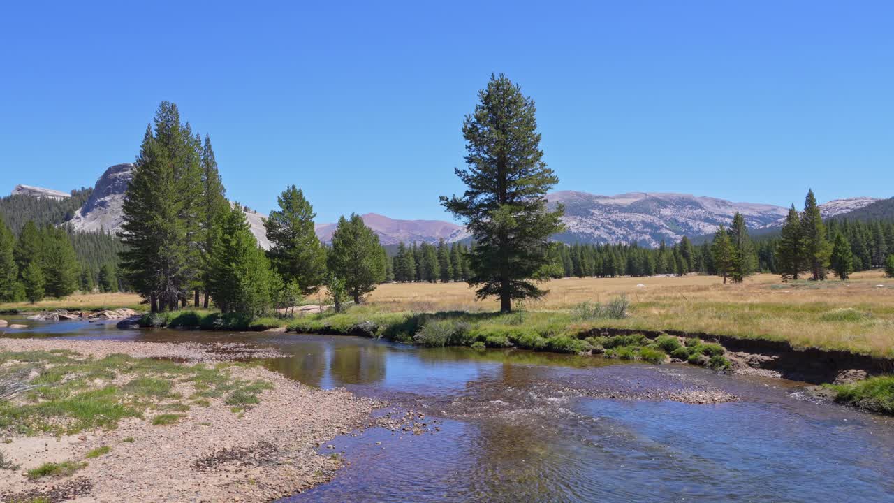 The Tuolumne River gently flows through the frame with the majestic granite mountains of the Sierra Nevada rising in the background