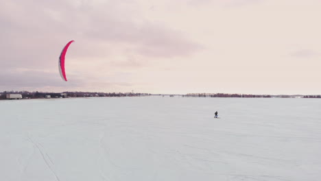 4k aerial winter extreme sport snow kiting competition race with different colorful snow-kites, ski, snowboarders over the ice lake in front of city at blizzard and snow weather from drone